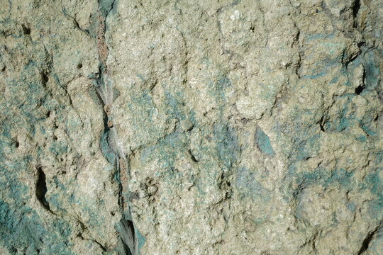 an uneven stone surface characterized by a unique pale green and teal patina. The texture is porous and crumbly.