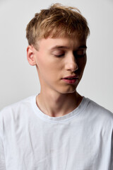 Fototapeta premium Calm, serene youth with a soft gaze and eyesclosed, wearing a plain white shirt. A minimalist studio setting uses soft lighting to convey contemplation, gentle mood, and quiet confidence in a clean,