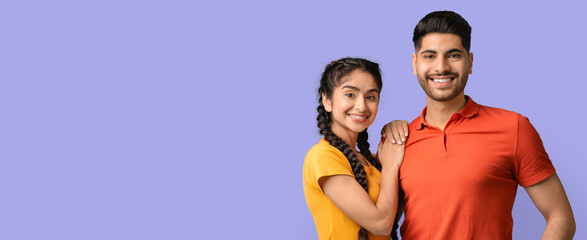 Two young adults are standing close, smiling brightly. The woman has long braids and wears a yellow top, while the man wears a red polo shirt. They appear joyful and carefree.