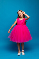 Cute happy little girl in a pink fluffy princess dress has fun and posing on blue background. Kids Birthday party celebration concept. Happy Birthday, copy space. High quality photo