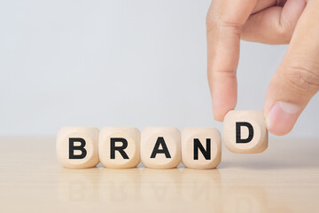 Businessman hand holding wooden cube block with BRAND business word on table background. Marketing, Advertising and Product development concept