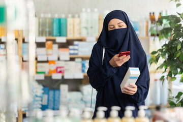 Selective young Muslim woman client scanning QR code on cream in chemist's shop
