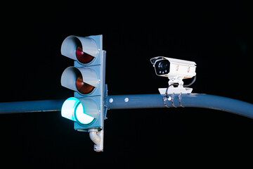 Traffic light displaying green signal with red signals above, accompanied by surveillance camera mounted on pole, representing urban safety and traffic management technology