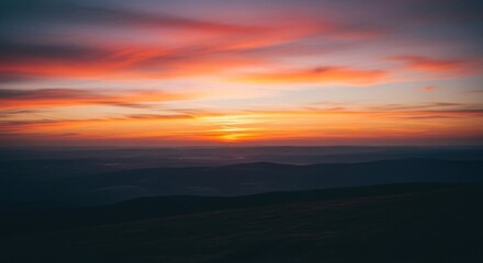 Fototapeta premium Vivid sunset sky ablaze with fiery oranges, reds, and yellows, painting the cloudscape above silhouetted mountain ranges in a tranquil, breathtaking vista, capturing the essence of dusk.