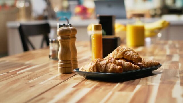 Empty kitchen table with croissants and homemade food for breakfast, contemporary apartment. Bright space with stylish kitchenware, fresh fruits and condiments on the counter, cozy home.