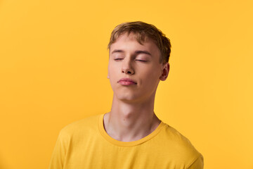 Fototapeta premium Calm, relaxation, serenity, yellow, closed eyes, peaceful, studio, emotion, simplicity, monochrome mood with a relaxed youth on a warm yellow backdrop, conveying stillness, inner balance, and gentle