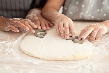 Two children are busy in the kitchen, rolling dough and using metal cookie cutters to create fun shapes. Flour covers their hands and the table, making the activity playful and joyful.