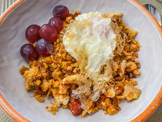 Traditional Spanish Migas (fried breadcrumbs) served with red grapes and a fried egg. Rustic Shepherd's style crumb dish close-up.