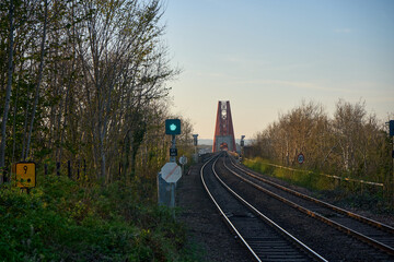 A quiet track leads to the iconic Forth Bridge, framed by trees at golden hour.