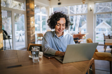 Fototapeta premium Woman working remotely on laptop in cafe
