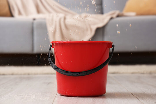 Water dripping from ceiling into plastic bucket on floor in living room, closeup