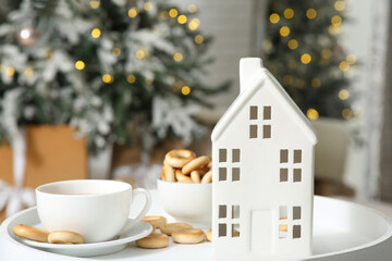 Candle holder in shape of house with tea cup and tasty bagels on coffee table near Christmas tree