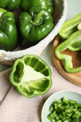 Wicker basket and bowl with fresh bell peppers on green wooden background, closeup