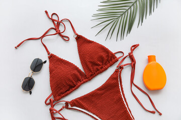 Stylish swimsuit, sunglasses and bottle of sunscreen cream on white background, closeup