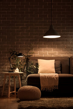 Stylish interior of living room with comfortable sofa, pouf and glowing lamps