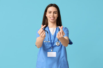 Young female doctor making heart gesture on blue background