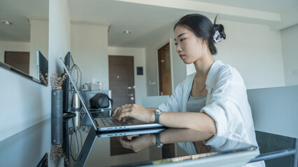 Pretty cheerful Asian girl working on laptop while sitting at home