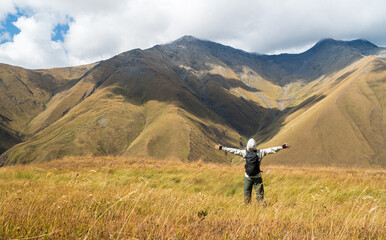 Hiker raising arms in victory while facing breathtaking mountains near Juta Village, Georgia. Symbol of success, freedom, and achievement in nature.