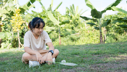A girl sitting on the grass looking at a badminton shuttlecock in a green outdoor garden.