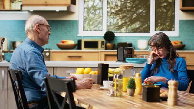 Mature wife appears overwhelmed and uninterested with silent irritation while her husband talks, creating candid marriage moment in retirement. Uninterested detached woman, melancholy. Camera B.