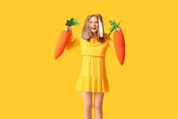 Happy woman in bunny ears with toy carrots on yellow background. Easter celebration