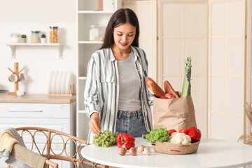 Young Asian woman unpacking fresh products from market at table in kitchen