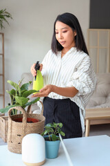 Young Asian woman watering plant at home office