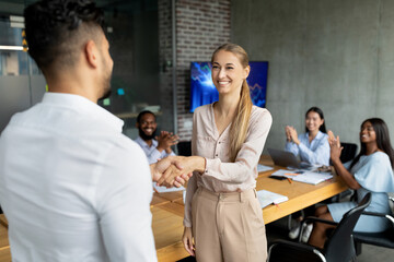 In a modern office setting, a male boss shakes hands with a new female employee while coworkers applaud. The atmosphere is welcoming and positive, encouraging teamwork and collaboration.