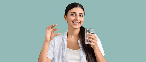 Young woman with vitamin E pill and glass of water on green background