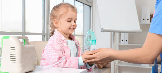 Fototapeta premium Female pediatrician with nebulizer and little girl in clinic