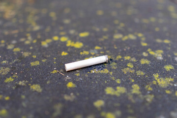 A cigarette butt is laying on the ground. It is white and has a small hole in it