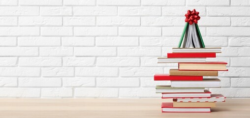 Christmas tree made of books on table against white brick background with space for text