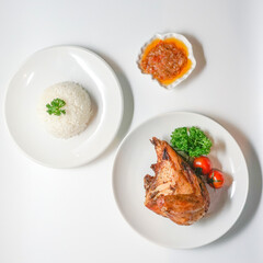 Top view of roasted chicken breast quarter served with steamed white rice, chili sambal sauce, parsley, and cherry tomatoes on white background. Clean Asian food image for menus, ads, and recipes
