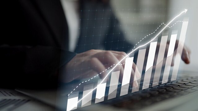 A business professional focuses on financial data using a laptop in an office. A chart overlay illustrates growth and success trends. Ideal for finance and business. Copula - Powered by Adobe