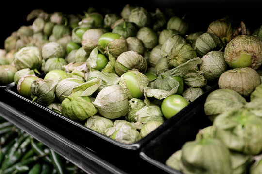 Fresh green tomatillos at grocery market display. Raw Mexican husk tomatoes in black plastic crates. Natural food ingredient for cooking. Healthy vegetable shopping scene. Close view of ripe tomatillo