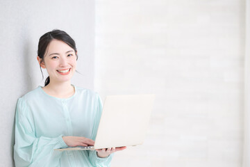 壁際でパソコンを操作するカメラ目線のかわいい女性