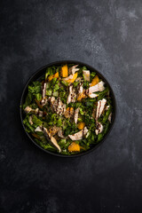 Fresh lettuce salad with roasted turkey and mango served on a dark black background