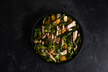 Fresh lettuce salad with roasted turkey and mango served on a dark black background