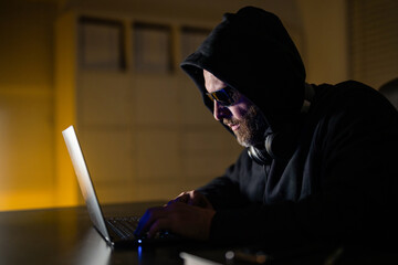 Hacker attack. Hacker gamer at night in office. Cyber attack. Cyber criminal and stolen financial data. Digital money thief. Hacker programmer in hoodie at office laptop, gaming. System infiltrator