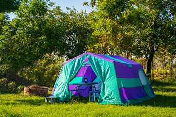 Camping tents at morning, vintage cabin tents, antique oil lamps, retro chairs, and a group of camping tents with outdoor coffee-making facilities on wooden tables in a forest camping area.