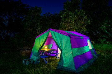 Nighttime camping tent in a forest clearing surrounded by nature