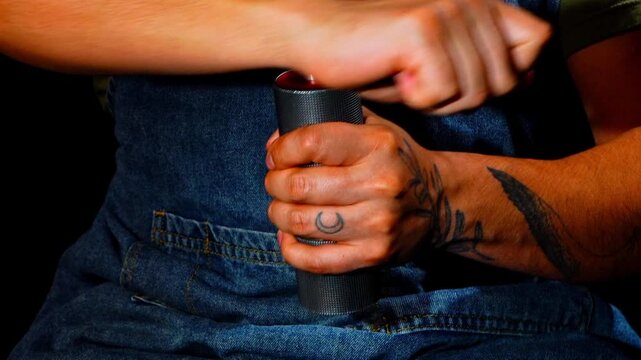 Cinematic slow motion close up of male barista hands with tattoos grinding fresh coffee beans with manual grinder. High speed capture showing muscle tension and mechanical detail in dark studio.