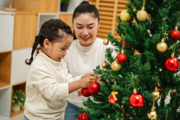 mother and toddler girl decorating Christmas tree with toy ball at home