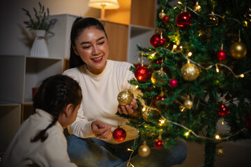 mother and toddler girl decorating Christmas tree in home at night