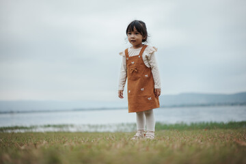 happy toddle girl standing on grass field near the river