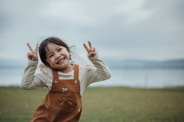 happy toddle girl making peace signs on grass field near the river