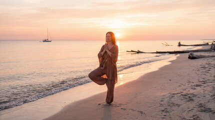 Woman practicing tree pose yoga meditation on peaceful beach at sunset sunrise