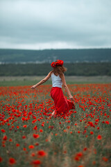 Woman poppies field running freely through vast spring flowers and dramatic sky