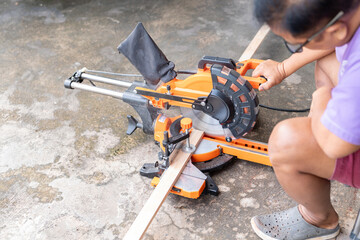 High-angle shot capturing a person using an electric orange and black sliding compound miter saw to cut a wooden plank.