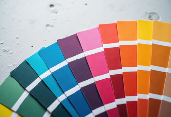 Obraz premium Color guide close up. Assortment of colors for design. Colors palette fan on a white concrete wall background. Graphic designer chooses colors from the color palette guide. Coloured swatches catalogue